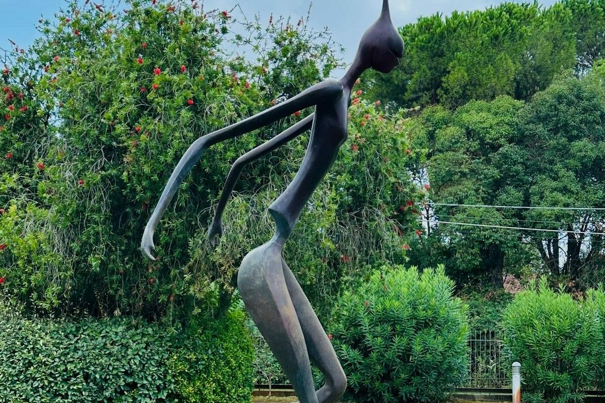 Nella foto c'è un prato verde con una statua in bronzo di forma simil umana che mima la corsa.